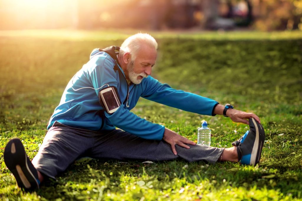Full length portrait of happy senior man in sportswear stretching in the park.