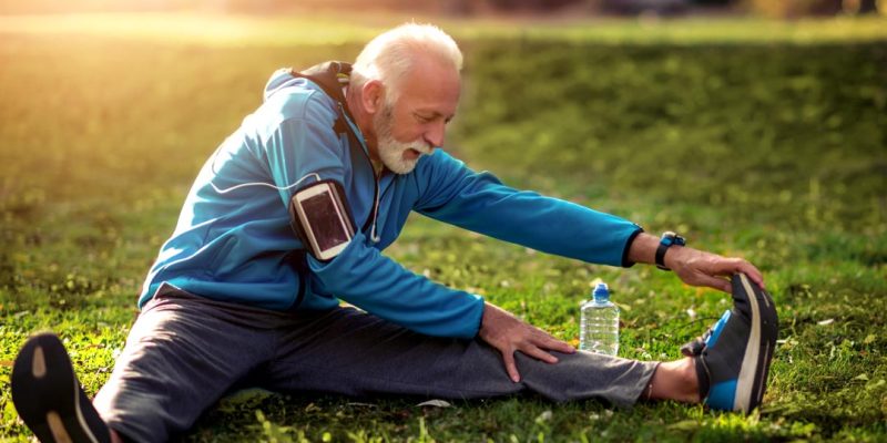 Full length portrait of happy senior man in sportswear stretching in the park.