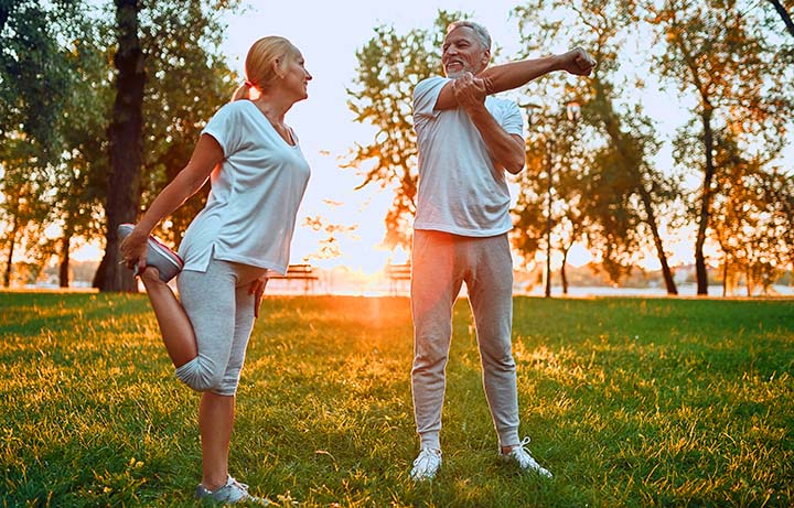Senior couple is doing sport outdoors. Stretching in park during sunrise.