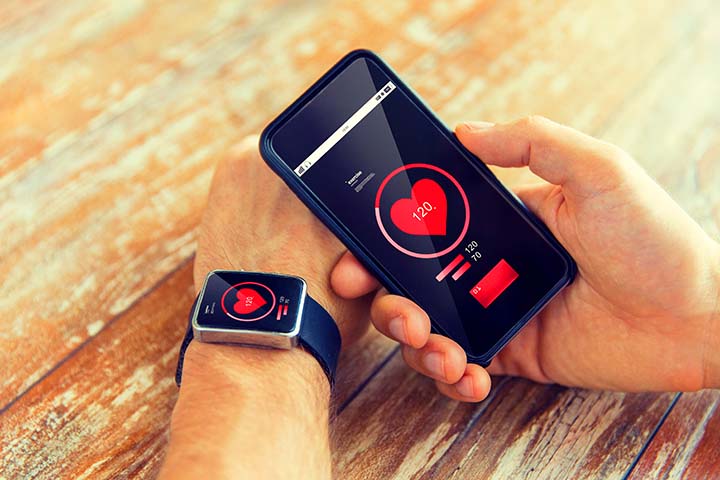 technology, health care, application and people concept - close up of male hand holding smart phone and wearing smart watch with red heart icon on screen and measuring pulse