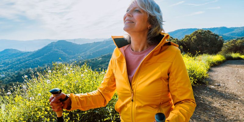 Woman hiking mountain trail with poles in sunshine