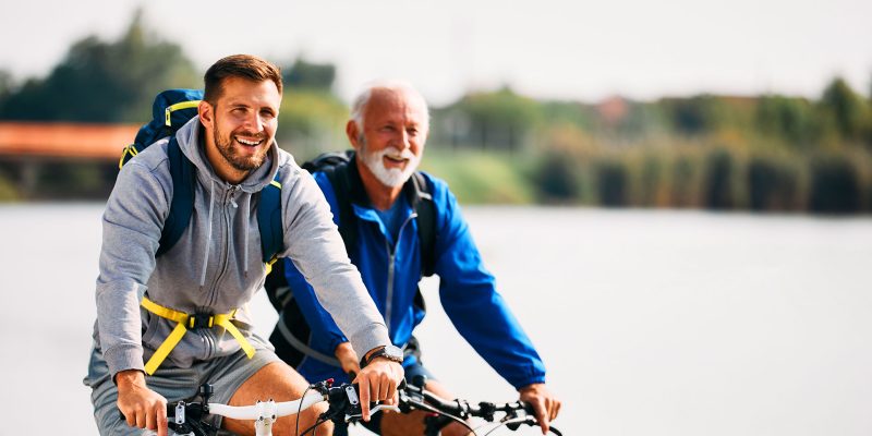 Father and son cycling together along riverside path