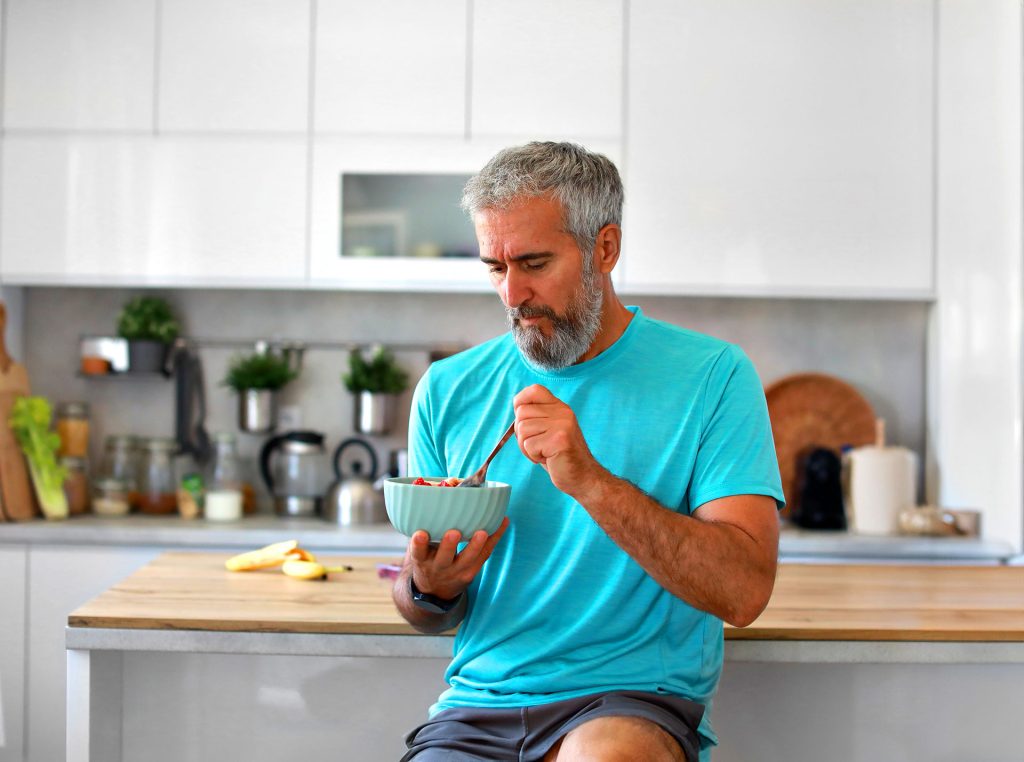 Mature man eating a healthy bowl of yogurt and fresh berries in a modern kitchen, no Heart Disease
