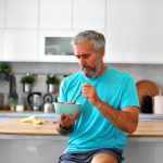 Mature man eating a healthy bowl of yogurt and fresh berries in a modern kitchen, no Heart Disease