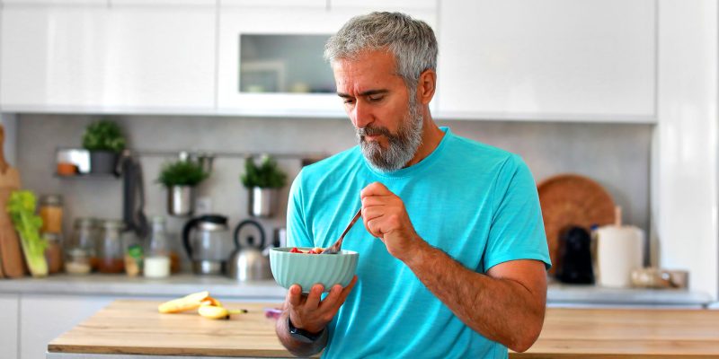 Mature man eating a healthy bowl of yogurt and fresh berries in a modern kitchen, no Heart Disease
